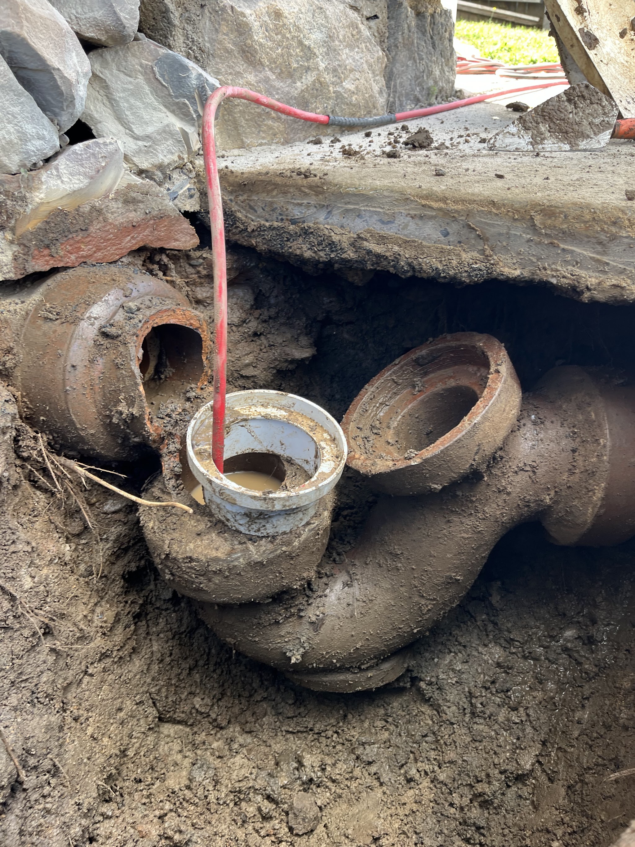 Excavated cast iron sewer junction with a jetting hose fed into the inspection opening