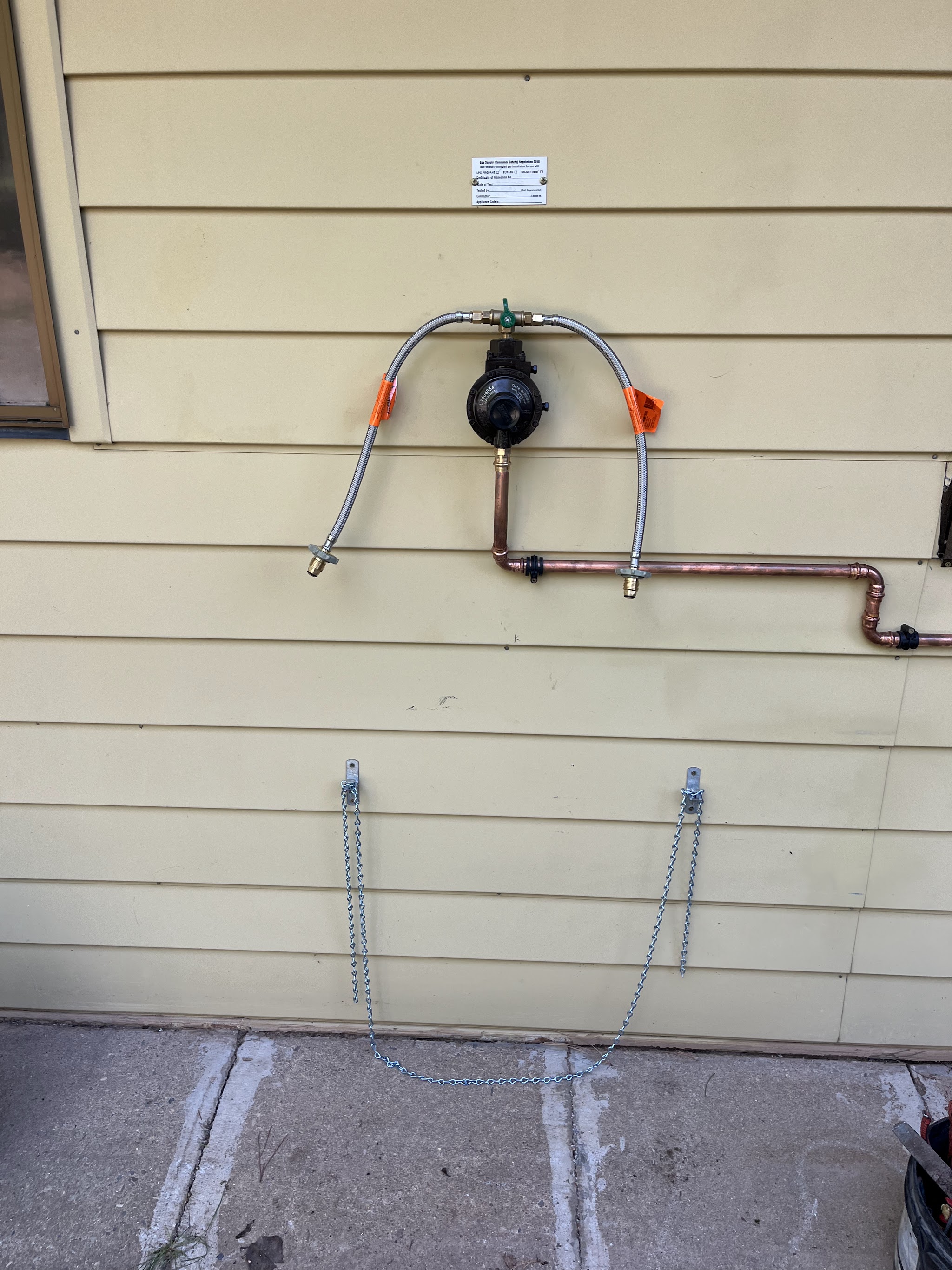 LPG regulator and copper gas line installed on a house wall below its compliance plate