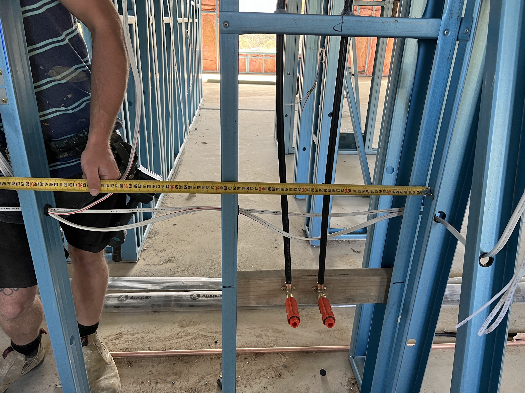Rough in plumbing being measured off a steel wall frame on a new build